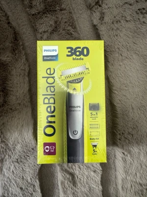 Philips OneBlade 360 trimmer - Philips OneBlade 360 är en elektrisk trimmer med 5-i-1 justerbar kam, body kit och 5 blad. Den har en svart och silver design och levereras i en gul förpackning. Perfekt för att trimma, styla och raka både ansikte och kropp. USB-laddning och vattentålig. X 5 blades!!