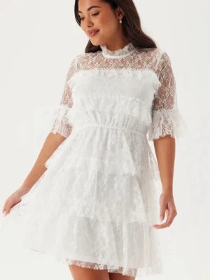 Vit spetsklänning med volanger - Superfin vit kort klänning i spets med volangdetaljer och halvtransparent överdel. Klänningen har korta ärmar, hög hals och flera lager spets som ger en romantisk look. Perfekt för dig som vill sticka ut med en söt och trendig stil. Bara använd 1 gång 💕Dock har den smink fläk längst kraken men inget synligt när man har på sig den.