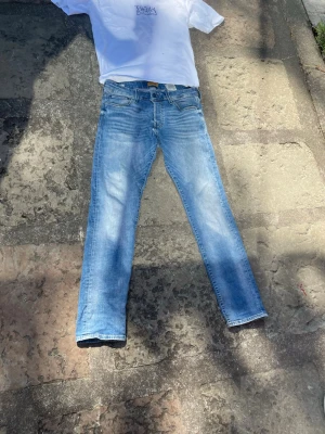 Ljusblå raka jeans från Jack & Jones - Säljer ett par ljusblå jeans från Jack&Jones med klassisk femficksdesign och slimmade ben. Jeansen har en snygg tvätt med slitningar och är tillverkade i bomull. Perfekta för en avslappnad och trendig still.