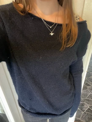 Mörkblå stickad oneshoulder  tröja -  Mörkblå stickad tröja med bred, något off-shoulder halsringning. Tröjan har långa ärmar och en avslappnad passform, perfekt för lager-på-lager. Enkel och stilren design som passar till det mesta.