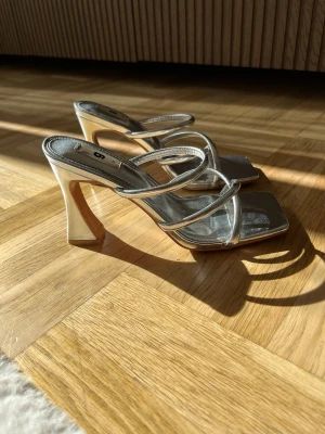 Silvriga klackar med ganska bred klack  - Snygga silvriga klackar från Gina Tricot med fyrkantig tå och tre tunna remmar över foten. Klacken är bred och stabil. Använt ett fåtal gånger. 