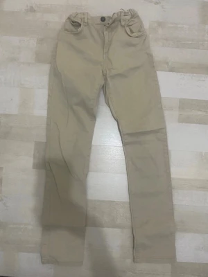 Beiga chinos med raka ben - Snygga beiga chinos med raka ben och klassisk passform. Byxorna har framfickor, bakfickor och hällor för bälte. Perfekta för en clean och stilren look. Materialet känns mjukt och bekvämt, passar till många olika outfits.