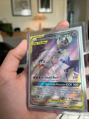 Pokémonkort Solgaleo & Lunala GX - Säljer ett Pokémonkort Solgaleo & Lunala GX TAG TEAM med 270 HP. Kortet har holografisk yta och färgstark design med motiv av Solgaleo, Lunala och Lillie. Kortet är på engelska och ligger i ett plastfodral.