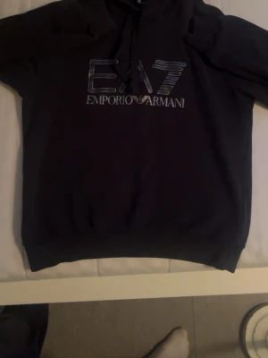 Emporio Armani EA7 hoodie - Svart hoodie från Emporio Armani EA7 med stor logga på bröstet. Storlek M i fint skick.