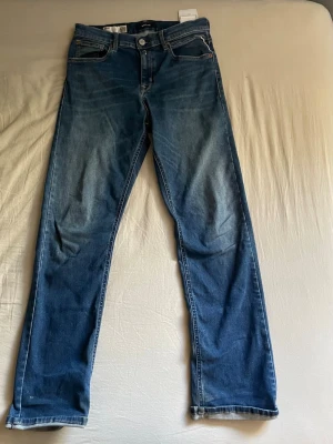 Replay Jeans - Säljer ett par klassiska blå Replay jeans i modellen Thad med fem fickor och snygg slitning framtill. Jeansen har normal midja, dragkedjegylf och är tillverkade i denim. Perfekta för dig som gillar en tidlös och avslappnad stil.