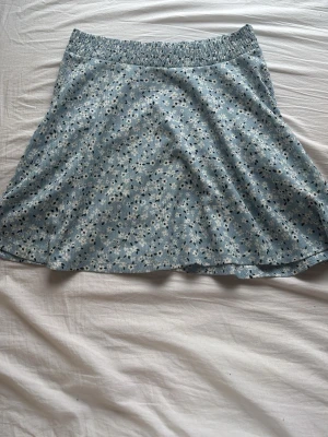 Blommig blå kortkjol från 157 - Supersöt blå kortkjol från 157 med små vitsvarta blommor. Kjolen har resår i midjan för skön passform och är gjord i ett mjukt, lätt material. Perfekt för dig som gillar en avslappnad och trendig stil.