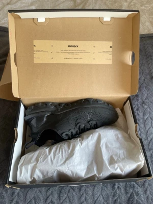 Svarta Nike react sneakers - Snygga helsvarta Nike D/MS/X sneakers med låg profil och sportig design. Skorna har en ventilerande mesh- och syntetöverdel, robust sula och klassisk snörning. Perfekta för dig som gillar streetwear och vill ha en clean look.