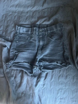 Högmidjade jeansshorts med fransar - Snygga högmidjade jeansshorts i svart denim med råa, fransiga kanter. Klassisk femficksmodell med knapp och dragkedja framtill. Perfekta för sommaren och ger en avslappnad vibe. Använda ganska mycket för något år sedan. Är i storlek 158/164💓vet ej vilket varumärke det kommer ifrån💓
