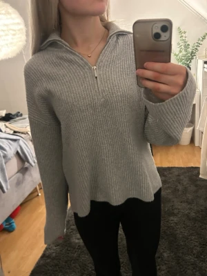 Ljusgrå stickad tröja med dragkedja - Mysig ljusgrå stickad tröja med halv dragkedja framtill och krage. Tröjan har en avslappnad passform, ribbstickat material och långa ärmar. Perfekt för lager på lager och enkel att styla till olika outfits. Endast använd fåtal gånger 
