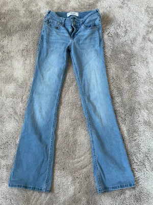 Bootcut jeans från Hollister ljusblå - Säljer ett par ljusblå bootcut jeans från Hollister med klassisk femficksmodell och låg midja. Jeansen har dragkedjegylf och är tillverkade i mjuk denim med lätt tvättad look. Perfekta för en avslappnad och trendig stil. Passar xs-s