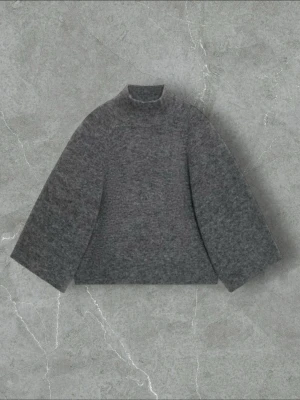 Grå stickad polotröja - Mysig grå stickad tröja med hög krage och vida ärmar. Tröjan har en rak passform och är tillverkad i ett mjukt, ull-liknande material som passar perfekt för kyliga dagar. Enkel och stilren design utan synliga detaljer eller mönster.