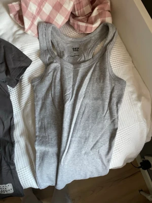 Grå linnetopp från 157 - Säljer en enkel och stilren grå linnetopp från 157. Toppen är ärmlös och har en rundad halsringning. Tillverkad i mjuk bomullsmix med 90% ekologisk bomull och 10% viskos. Perfekt att matcha med jeans eller shorts.