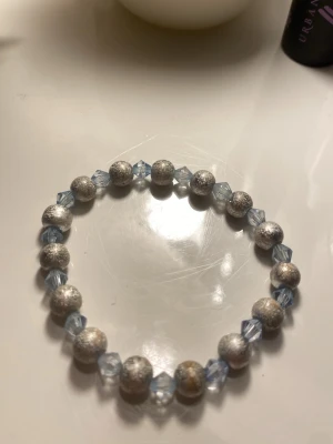 Elastiskt armband med silver- och blå pärlor - Snyggt armband med glittriga silverfärgade runda pärlor och facetterade ljusblå pärlor. Lite slitet men fortfarande snyggt 💗