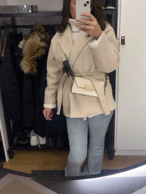 Beige kappa, Missäy - Stilren beige kort kappa med knytskärp i midjan. Den passar till många olika outfits och är snygg att ha till vardags. Har använt den ett par gånger men den ser ut att vara ny. Den passar dig i strl Xs och S ganska bra hade jag sagt och är allmänt väldigt fin. Den är köpt på Missäy.