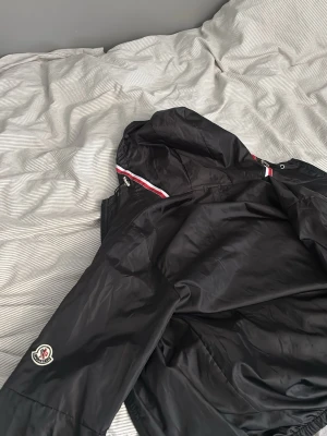 Svart vindjacka  - En svart vindjacka med huva och dragkedja fram till, även till fickorna. Tillverkad i lätt och glansigt material som passar perfekt för blåsiga dagar under sommaren. Köptes på Plick, säljs pga för liten för mig. 