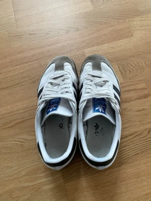 Adidas Originals vita sneakers - Klassiska Adidas Originals sneakers i vitt med svarta ränder och grå mockadetaljer på tån. Enlla att tvätta och i bra skick.