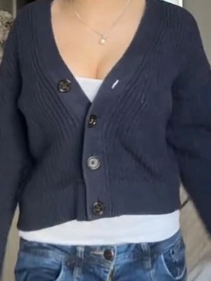 Mörkblå stickad kofta med knappar - Snygg mörkblå stickad kofta med v-ringning och stora knappar framtill. Kortare modell som passar perfekt till jeans eller kjol. Ribbstickade detaljer ger extra struktur och stil. Inget synligt märke.