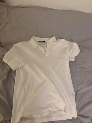 Vit piké från J.Lindeberg - Klassisk vit pikétröja från J.Lindeberg med krage och knappar framtill. Tillverkad i mjuk bomull som känns skön mot huden. Perfekt till jeans eller shorts för en clean och stilren look.