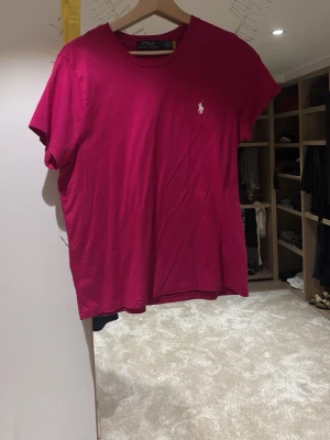 Rosa t-shirt från Polo Ralph Lauren - Säljer en klassisk rosa t-shirt från Polo Ralph Lauren med den ikoniska loggan broderad i vitt på bröstet. T-shirten har rund halsringning och korta ärmar. Tillverkad i mjuk bomull för skön känsla och enkel stil. Storlek L men skulle säga att de passar m med och s för en oversised look