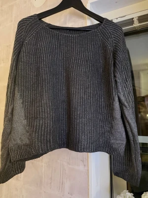 Silvrig tröja Gina Tricot - Snygg mörkgrå stickad tröja från Gina Tricot med rund halsringning och långa ärmar. Tröjan är tillverkad i en mjuk mix av 50% akryl och 50% bomull, vilket gör den både bekväm och mycket stretchig. Kan även passa Medium för en oversized look.