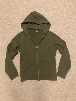 Olivgrön hoodie från Polo Ralph Lauren - Mörkgrön Ralph Lauren Hoodie i mycket bra skick! Tröjan har inga defekter och är i storlek XL för baran men sitter som en S, Personen på bilden är 180 cm som referens, hör av er om frågor!