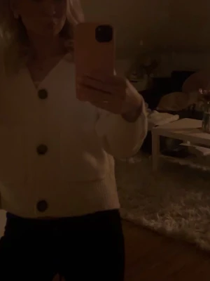 Vit stickad kofta från Vero Moda - Säljer en krämvit stickad kofta från Vero Moda med stora bruna knappar och två framfickor. Koftan har v-ringning, ribbade muddar och en avslappnad passform. Den blir lurvig lätt