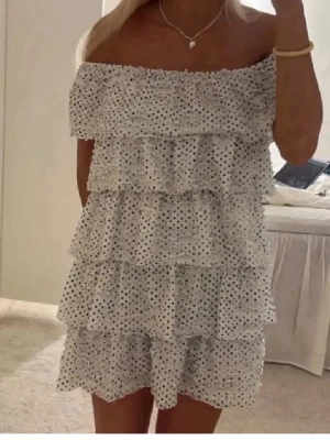 Vit prickig volangklänning - Supersöt kort vit klänning med svarta prickar och volanglager. Sjukt söt!! Den har ett svart hans runt magen som man även kan ta av om man vill❤️