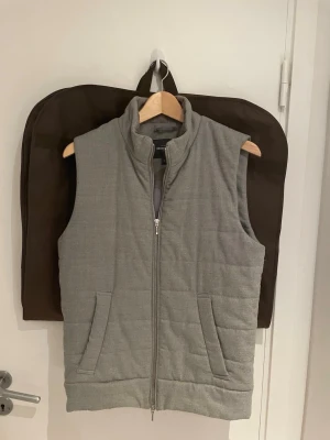 Grå quiltad dunväst från Dressmann - Säljer en stilren grå väst från Dressmann med quiltad design och dragkedja framtill. Västen har två fickor, hög krage i manchester och knappdetaljer i nederkant. Perfekt för lager-på-lager och enkel att matcha med olika outfits. Västen är i väldigt gott skick och har anväts med omsrog. Vid frågor? Eller funderingar tveka inte på att höra av dig! Mvh, Oscar 