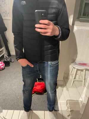 Svart pufferjacka med huva - Snygg svart cardiganjacka med quiltade partier och dragkedja framtill. Jackan har huva och långa ärmar i mjukt material, perfekt för lager på lager. Enkel och stilren design som passar till det mesta.                                                   Ny pris 499 kr Storlek 165 men är mer som xs.