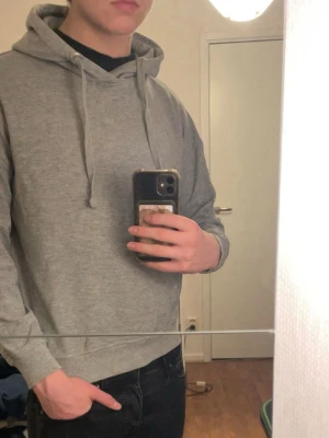Grå hoodie  - En enkel och stilren grå hoodie med huva och dragsnören. Hoodien har en avslappnad passform, ribbade muddar vid ärmslut och nederkant samt är tillverkad i mjukt sweatshirtmaterial. Perfekt för en chill och casual look.
