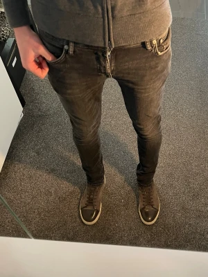 Svarta nudie jeans i modell skinny lin - Säljer ett par svarta skinny jeans med dragkedjegylf och klassisk femficksdesign. Jeansen har en tight passform och är tillverkade i ett stretchigt material som sitter snyggt. Perfekta för dig som gillar en slimmad look. Nudie jeans Skinny Lin