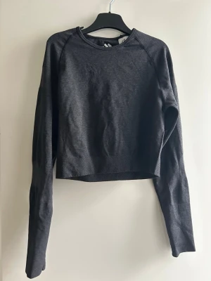 Mörkgrå croppad träningströja - Snygg mörkgrå croppad tröja med rund halsringning och långa ärmar. Tillverkad i ett mjukt och stretchigt material som passar perfekt till både chill och träning. 