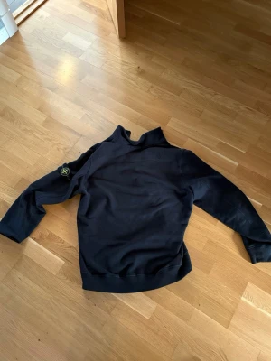 Svart half-zip hoodie från Stone Island - Svart hoodie från Stone Island med half-zip framtill och hög krage. Klassisk patch med logga på vänster ärm. Tillverkad i mjuk bomull, perfekt för en avslappnad och stilren look. Långa ärmar och ribbade muddar för extra komfort.