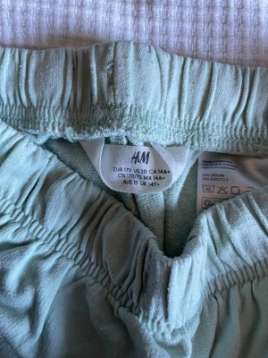 Ljusgröna shorts från H&M - Snygga ljusgröna shorts från H&M med elastisk midja och vita detaljer längs kanterna. Tillverkade i mjuk bomull, perfekta för varma dagar. Sportig design med avslappnad passform.