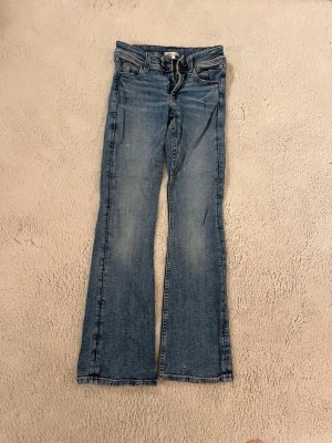 Blå bootcut jeans med dubbla knappar - Säljer ett par blå bootcut jeans med dubbla knappar i midjan och klassisk femficksdesign. Jeansen har en lätt look och raka ben som går ut något nedtill. Perfekta för en avslappnad och trendig stil.💖