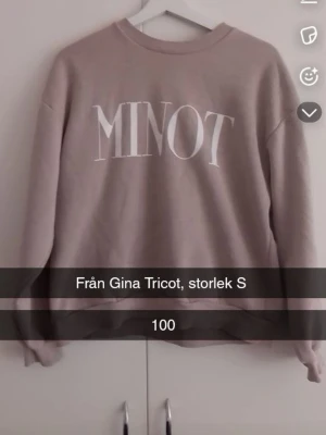 Beige sweatshirt från Gina Tricot - Säljer en beige sweatshirt från Gina Tricot med trycket 'MINOT' i vitt framtill. Tröjan har rund halsringning, avslappnad passform och ribbade muddar vid ärmslut och nederkant. Perfekt för en chill och stilren look.