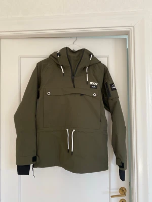 Olivgrön skidjacka från Dope - Dope anorak (halv dragkedja) jacka grön – storlek S (dam).  • Modell ”Annok W” i färgen olive grön - googla om man vill se hur jackan sitter på hemsidans modeller. • Mellanvikts vaddering för perfekt balans mellan värme och prestanda.  •	Skick: Nyskick. •	Detaljer: Magficka framtill, justerbar midja och huva. •	Perfekt som skid-/snowboardjacka eller vardagsjacka.  Köpt via Vinted, därför har jag tyvärr ingen mer info om modell/år.  📦 Skickas snabbt!