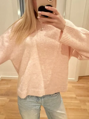 Ljusrosa oversized stickad tröja - Mysig ljusrosa stickad tröja med oversized passform och rund hals. Tröjan har långa ärmar och ribbade muddar vid ärmslut och nederkant. Perfekt för lager på lager och en avslappnad look.