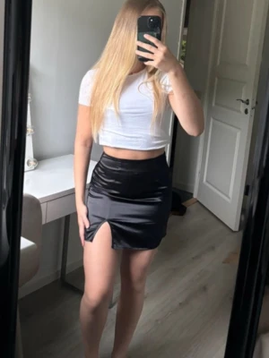 Svart kort satinkjol  - Aldrig använd, dragkedja och liten slits i sidan.