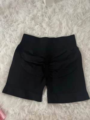 Svarta tighta shorts med scrunch - Säljer ett par svarta tighta shorts med scrunch-detalj bak som framhäver formen. De har hög midja och är tillverkade i ett stretchigt material som passar perfekt till träning eller chill. Stilrena och enkla att matcha med olika toppar.