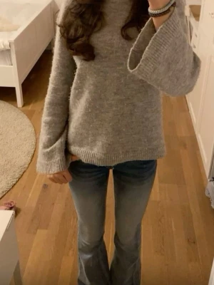 Grå stickad tröja med vida ärmar - Mysig grå stickad tröja med breda, vida ärmar och ribbstickade muddar. Tröjan har en avslappnad passform och är perfekt för att hålla sig varm under kyliga dagar. Materialet ser ut att vara mjukt och behagligt.