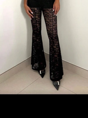 Svarta utsvängda spetsleggings - Säljer ett par svarta leggings i genombruten spets med utsvängda ben. De har hög midja och ett riktigt trendigt 70-talsinspirerat vibe. Perfekta för dig som vill sticka ut och älskar statement-plagg. Materialet är stretchigt och följsamt.
