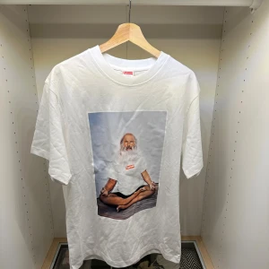  Supreme Rick Rubin Tee - 🔷 White T-shirt in a classic fit 🔷 🔷 Iconic graphic print from Supreme featuring a meditating figure 🔷 🔷 Clean and minimal base with a strong statement front 🔷 🔷 Soft cotton fabric for everyday comfort 🔷 🔷 Ribbed crewneck collar 🔷 🔷 Easy to style – works with both casual and streetwear outfits 🔷 🔷 Timeless piece with recognizable design 🔷