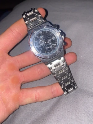 Silverfärgad klocka från Poedagar - Stilren klocka från Poedagar i silverfärgat rostfritt stål med svart urtavla och kronograf-detaljer. Klockan har en robust länkarmband och markerade skruvar på boetten för en sportig look. Vattentät till 3ATM och passar perfekt till dig som gillar klassisk design.