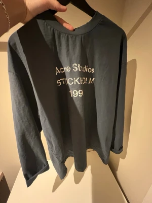Mörkblå långärmad Acne Studios tee - Snygg mörkblå långärmad t-shirt från Acne Studios med tryck i vitt på bröstet där det står 'Acne Studios STOCKHOLM 1996'. Tillverkad i mjuk bomull och har en relaxed fit med rund hals.