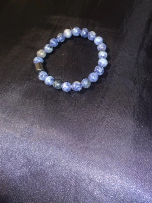 Blått pärlarmband med stenar - Snyggt armband med runda blå pärlor i olika nyanser, trädda på elastisk tråd. Pärlorna har en naturlig stenlook och armbandet har en metallisk detalj. Perfekt accessoar för att lyfta din stil med en cool touch. Pris diskuterbart