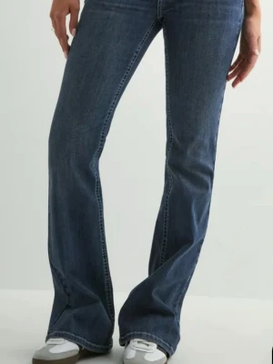 Mörkblå bootcut jeans  - Säljer ett par mörkblå bootcut jeans med klassisk femficksdesign och normal midja. Jeansen har en snygg utsvängd passform från knät och ner, vilket ger en retrovibe. Tillverkade i denim med lätt stretch för extra komfort. Original pris är 699