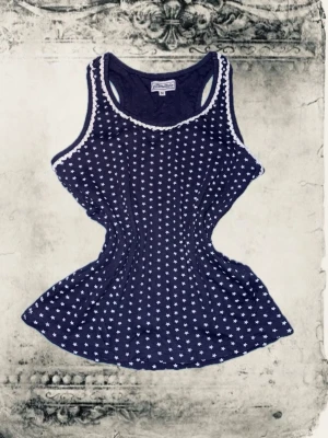 Mörkblå linnetopp med stjärnmönster - Supersöt mörkblå linnetopp med små vita stjärnor över hela och vit spetskant vid halsringningen. Perfekt till sommaren och lätt att styla med jeans eller kjol. Materialet känns mjukt och stretchigt, vilket gör den bekväm att bära hela dagen.