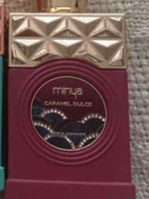 Minya Caramel Dulce parfym - Lyxig parfymflaska från Minya i en djup vinröd färg med guldfärgat lock och dekorativa detaljer. Flaskan har geometriskt mönster på locket och en elegant etikett med texten 'Caramel Dulce'. Perfekt för dig som gillar söta dofter och snygg design  ca 80% kvar .