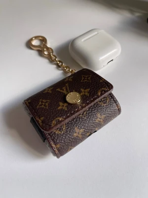  Vuitton monogram plånbok mini - Säljer en liten plånbok från  Vuitton i klassiskt brunt monogrammönster med guldfärgad knapp och kedja. Perfekt för småsaker eller som nyckelring. Tillverkad i tåligt läder med svart insida och präglad logga.